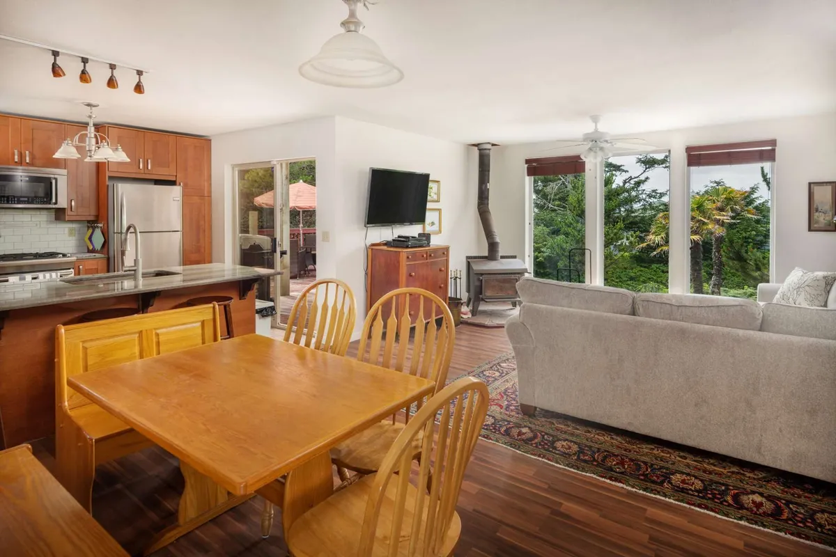 This bright, open-concept interior connects the dining area, kitchen island, and living zone. Large windows bring in ample light and provide tranquil views of the outdoors, while the arrangement of the dining table and sofa makes the space ideal for shared meals, games, and conversation.