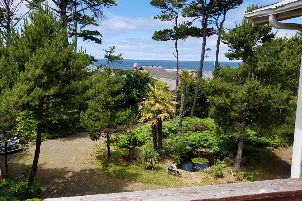 A lush garden scene with a tranquil pond bordered by tall trees and tropical plants, offering a view toward the ocean in the distance. The foreground invites relaxing by the water’s edge, birdwatching, and observing the interplay between forest and coastal environments.