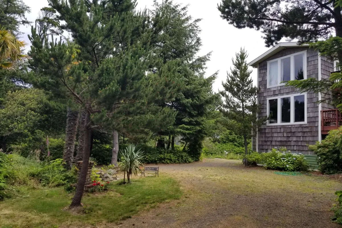 This exterior image highlights the home's woodland setting, featuring tall trees, a garden bench, and the house partially visible. The peaceful scene evokes the adventure of nature walks and the charm of garden relaxation.