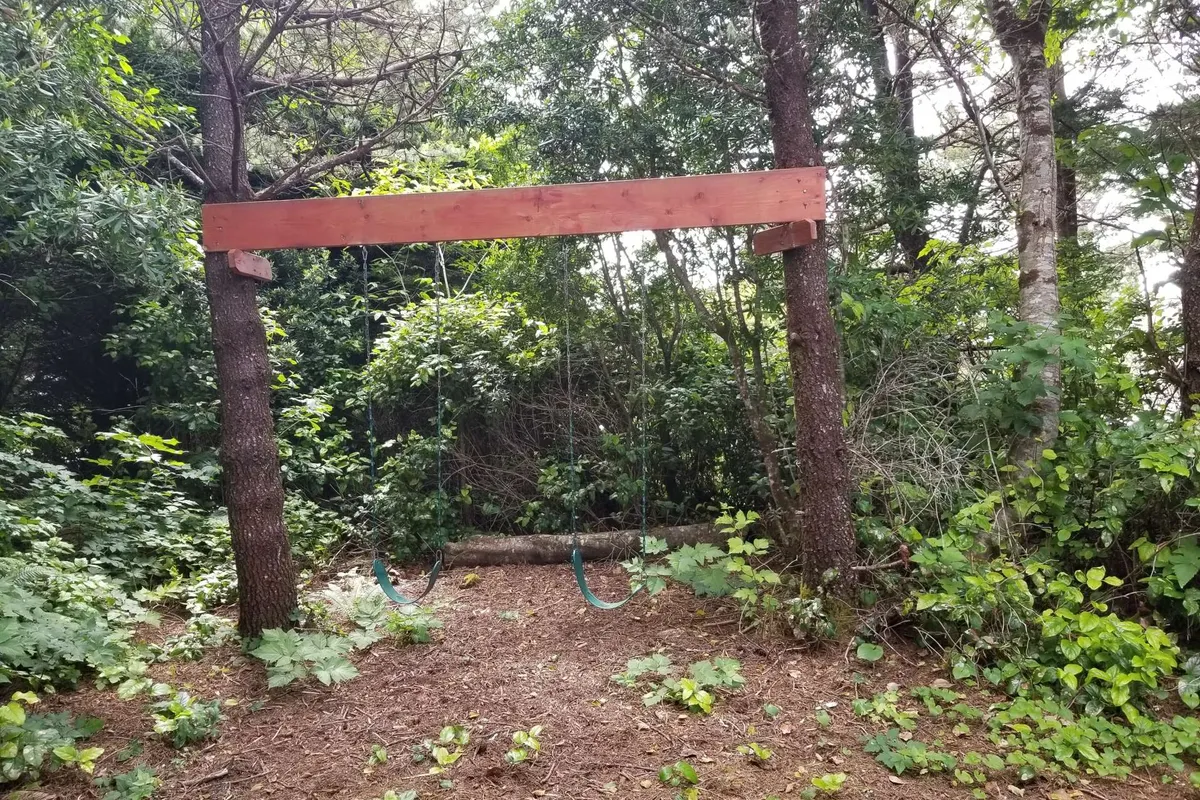 This image features a charming wooden swing set surrounded by lush greenery and an earthy ground, inviting families and children to play outdoors. The playful mood and visible swing make it clear that outdoor fun is a highlight here.