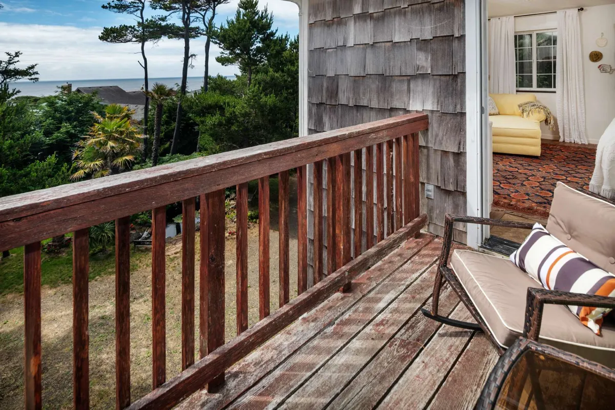 A serene balcony scene shows comfortable outdoor seating, a classic wooden railing, and a panoramic view of the ocean surrounded by lush greenery. The setup is perfect for group breakfasts, evening chats, or stargazing among the treetops.